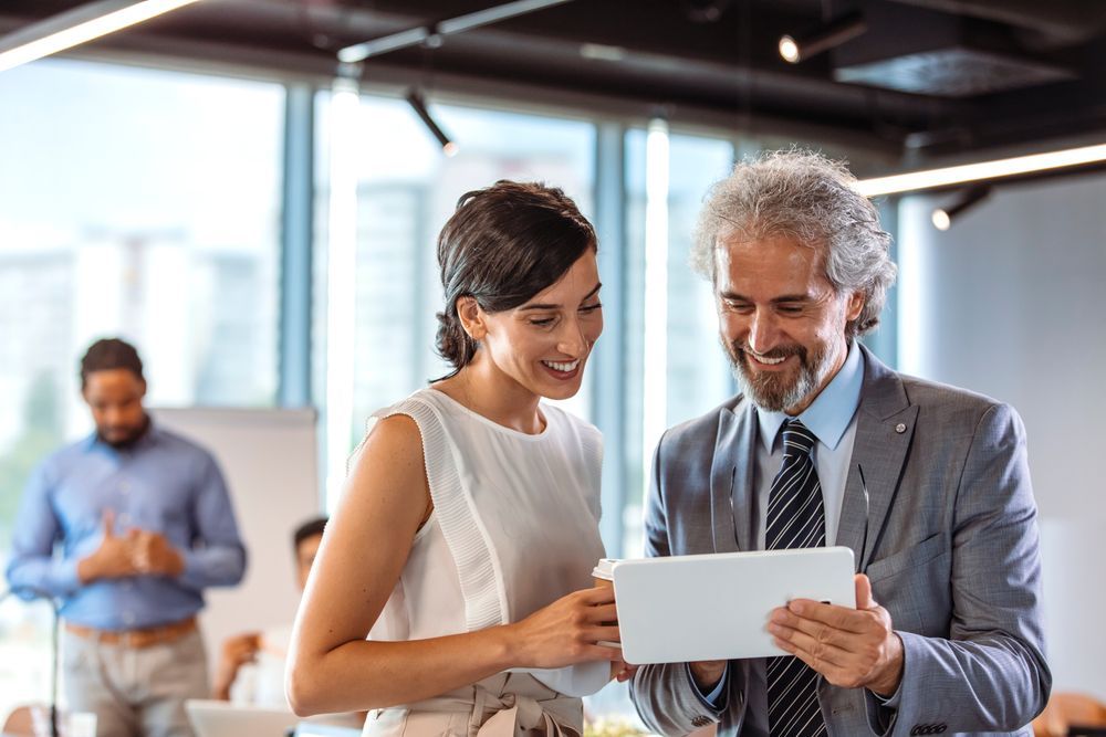 Two coworkers smiling and reviewing a tablet in a bright office