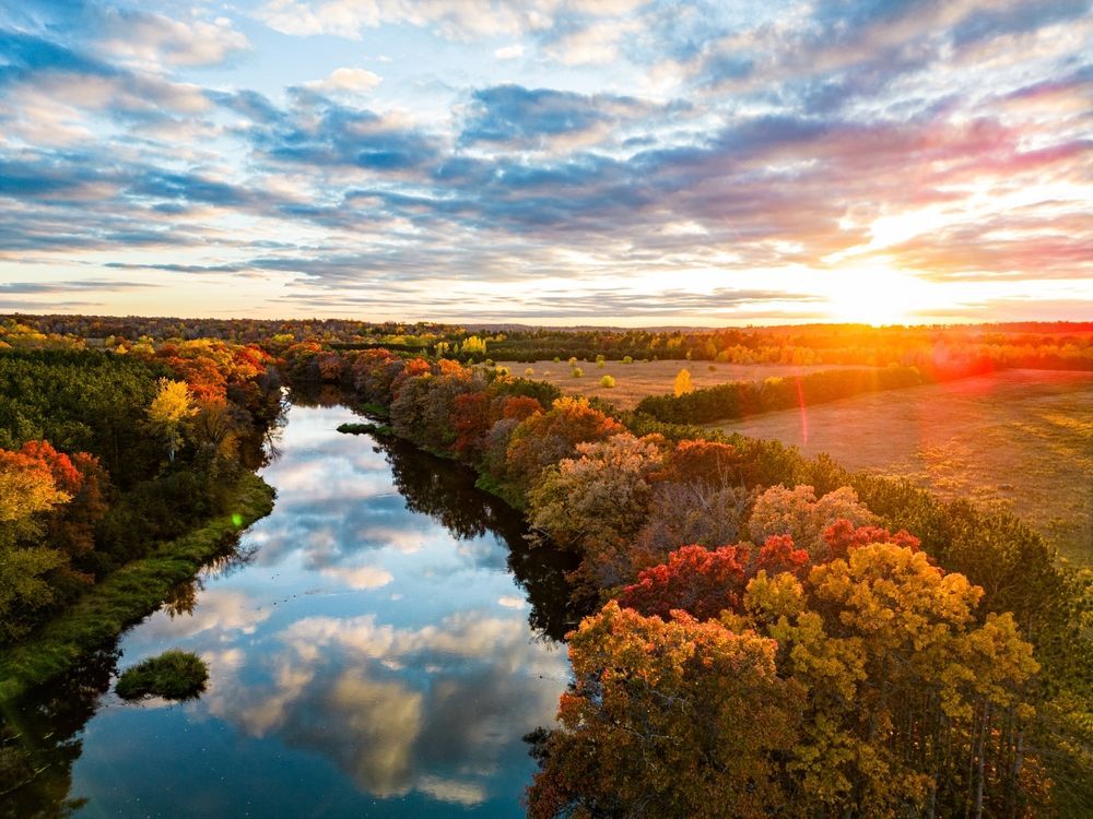 Sunset over a winding river reflecting clouds, surrounded by autumn-colored trees.