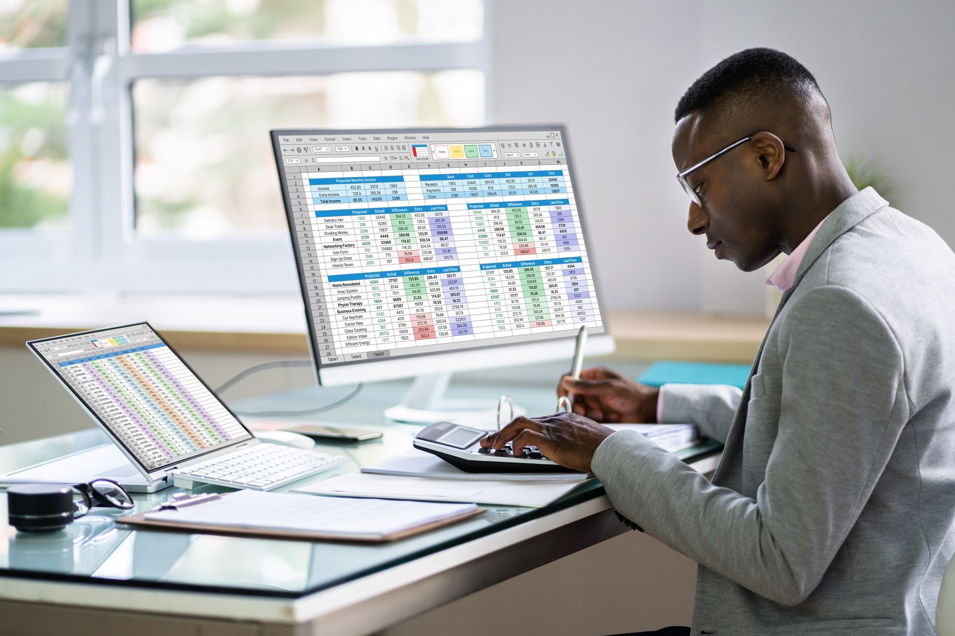 Person working on a laptop with a spreadsheet on a monitor at a bright desk