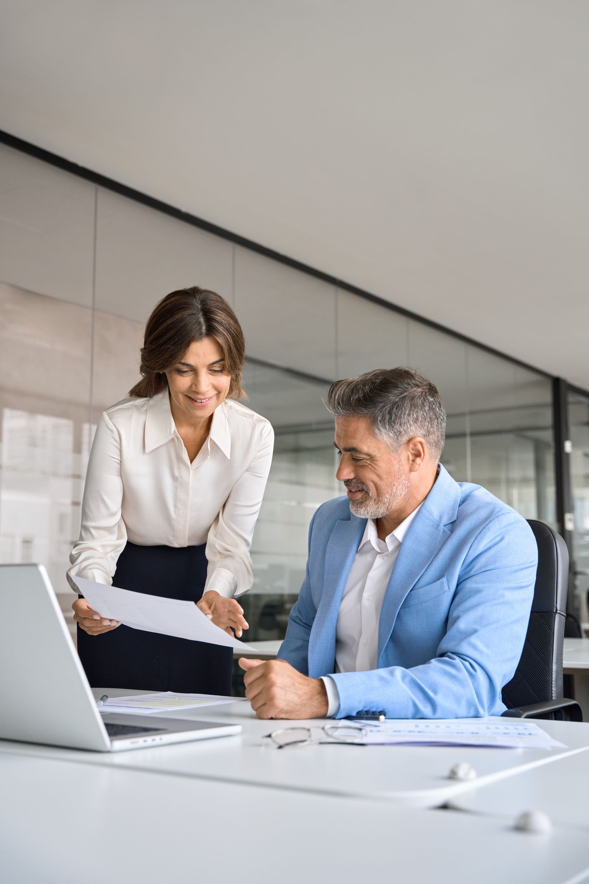 Two coworkers reviewing documents at a laptop in a modern office