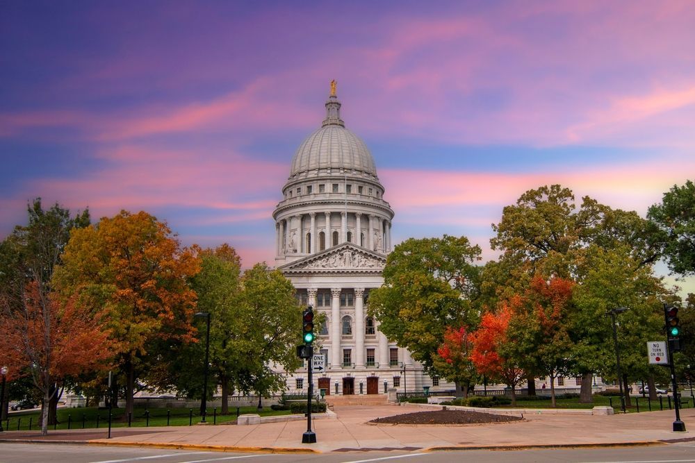 State capitol building with a domed dome framed by autumn trees under a pink sunset sky