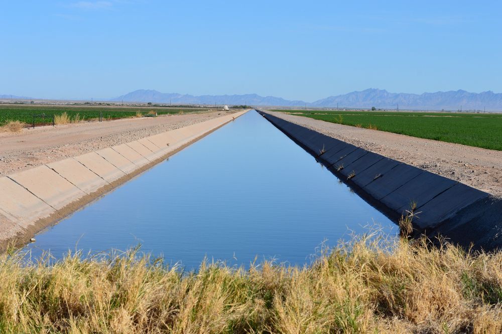 A concrete irrigation canal with still blue water stretching through flat farmland under a clear sky