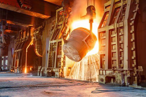 Molten metal pouring from a suspended ladle in an industrial foundry, glowing orange