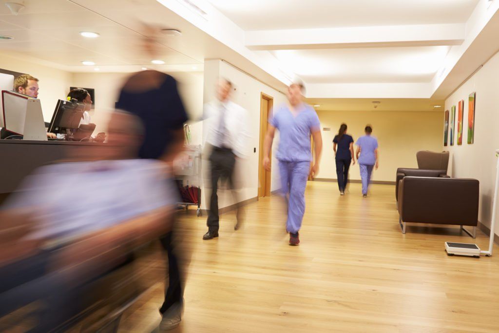 People walking through a bright hospital hallway, with a blurred person passing in the foreground.