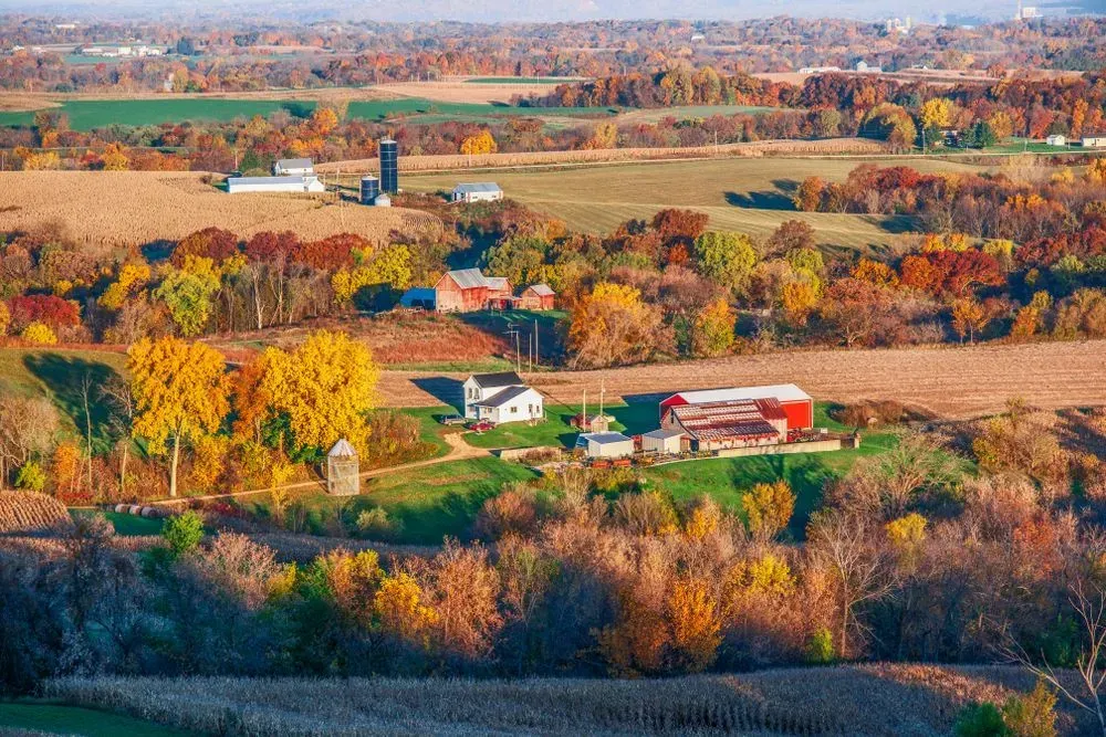 Autumn rural landscape with colorful trees, fields, and a few farm buildings under a clear sky