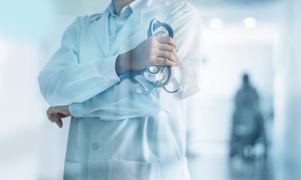 Doctor in a white coat holding a stethoscope in a bright hospital hallway