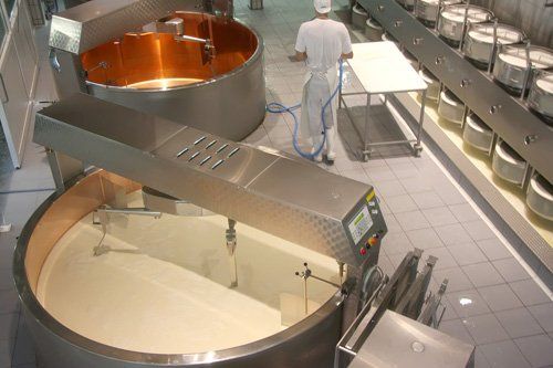 Large stainless-steel mixing vats in a food processing facility, with a worker standing nearby.