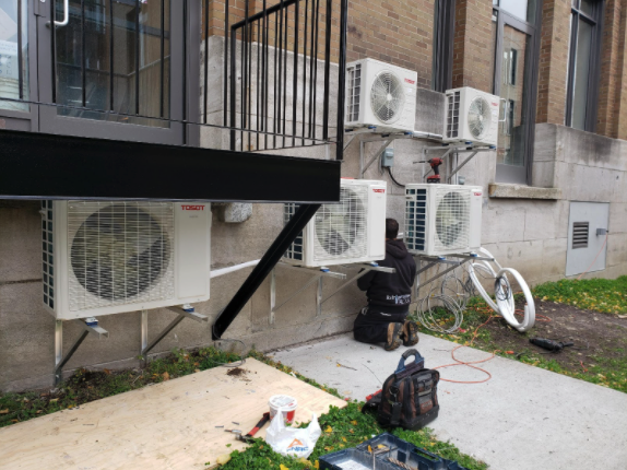 Un homme installe des climatiseurs sur le côté d'un immeuble.