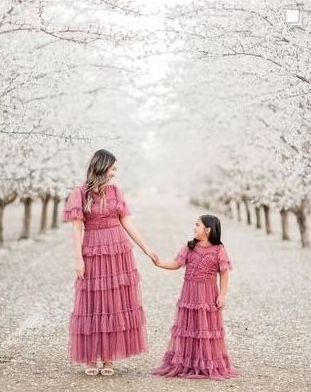 A mother and daughter are holding hands in front of a almond blossom orchard.