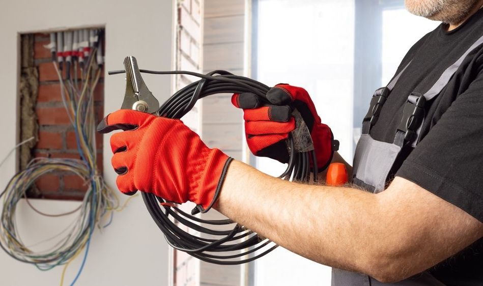 A man wearing red gloves is holding a wire and a pair of pliers.