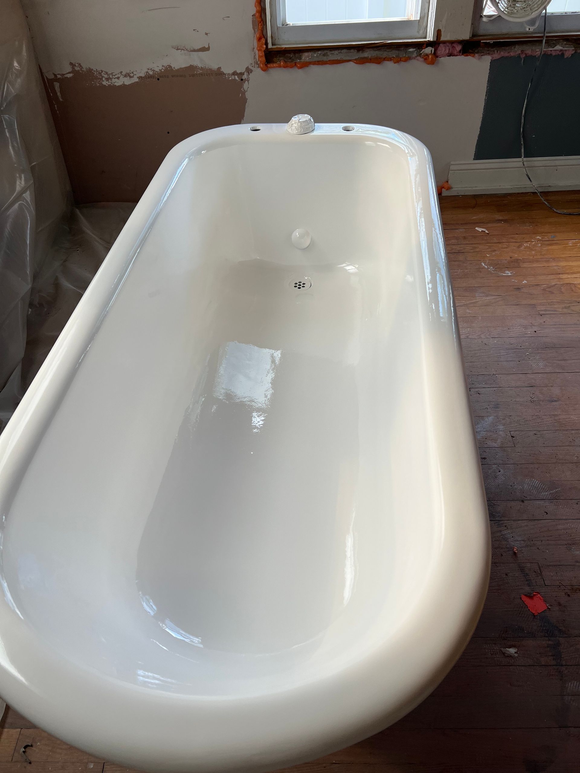 A white bathtub is sitting on a wooden floor in a bathroom.