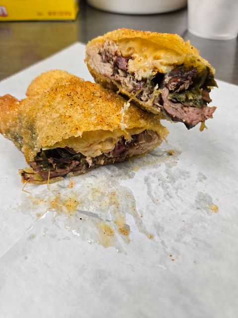 Two halves of a sandwich with golden bread and dark filling on white paper, one bite taken