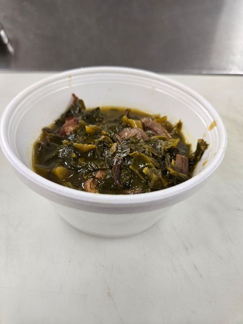 Small white cup of dark leafy stew on a white counter, with a stainless steel background