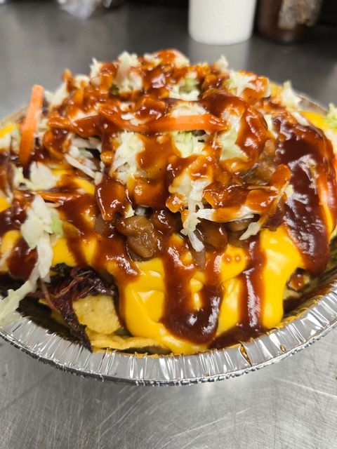 Foil tray of loaded fries topped with melted cheese, brown sauce, and shredded vegetables