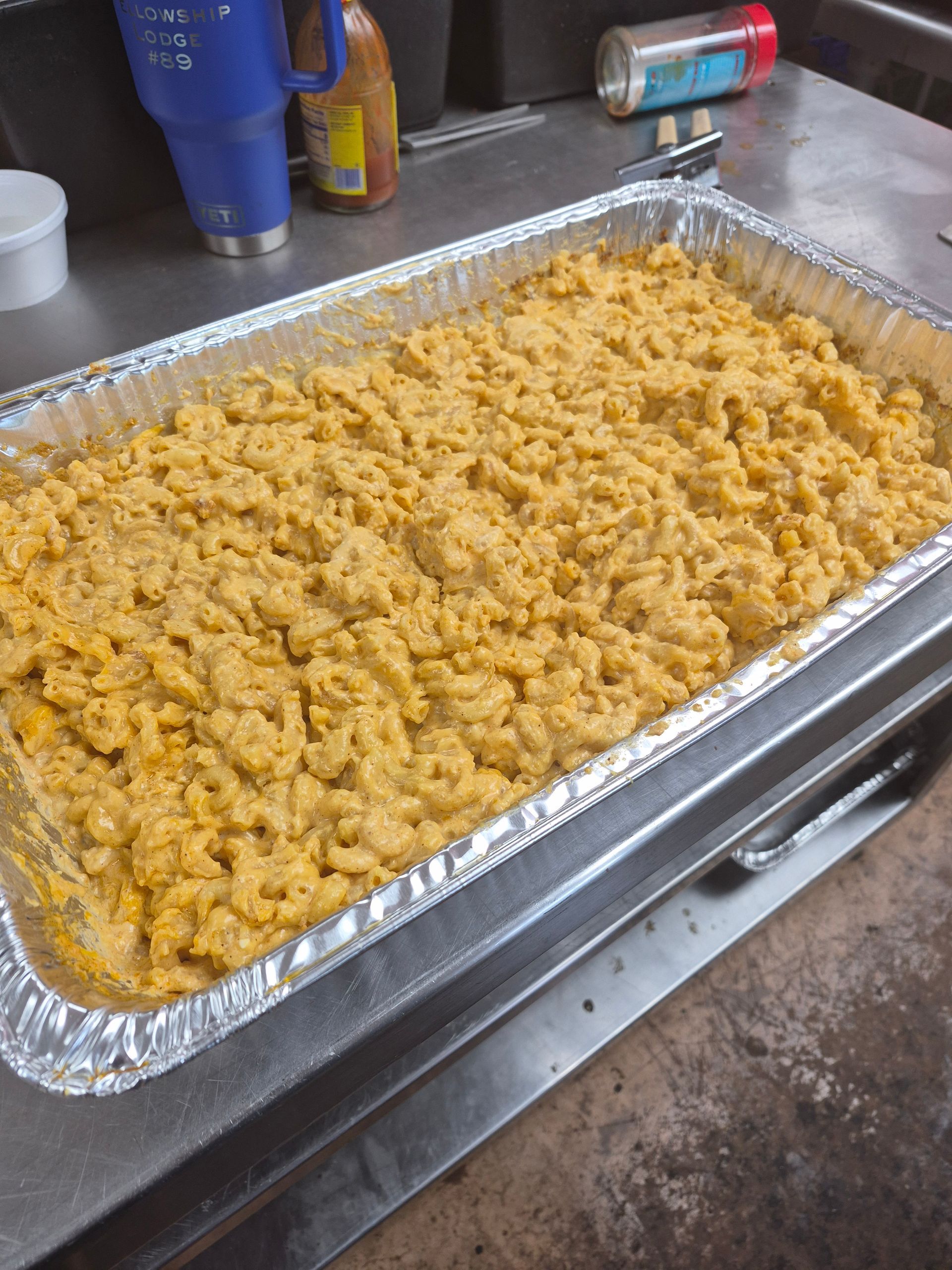 Tray of baked macaroni and cheese in a kitchen sink, with aluminum foil lining the pan.