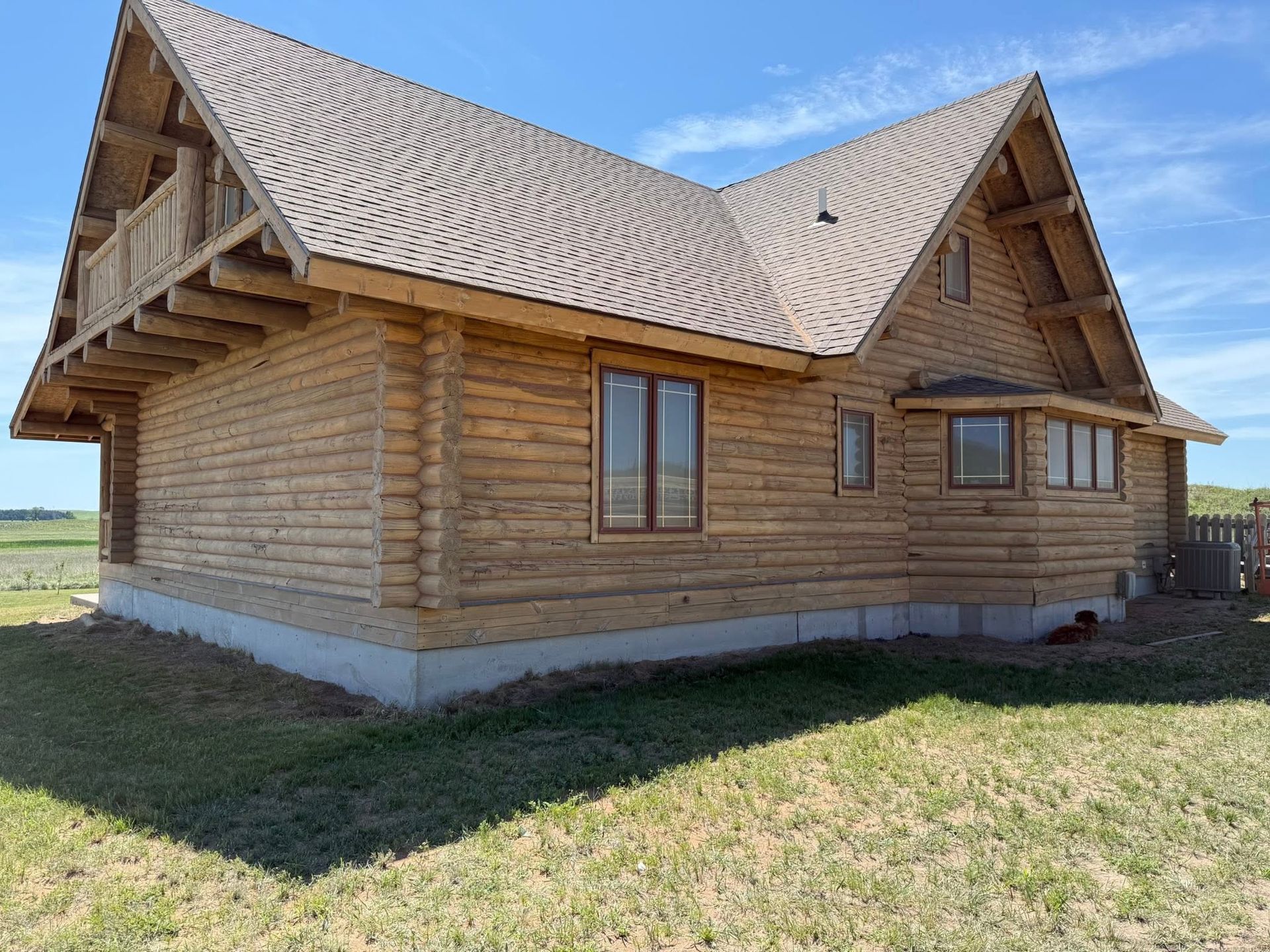 Log cabin-style house with a steep shingled roof in a grassy field