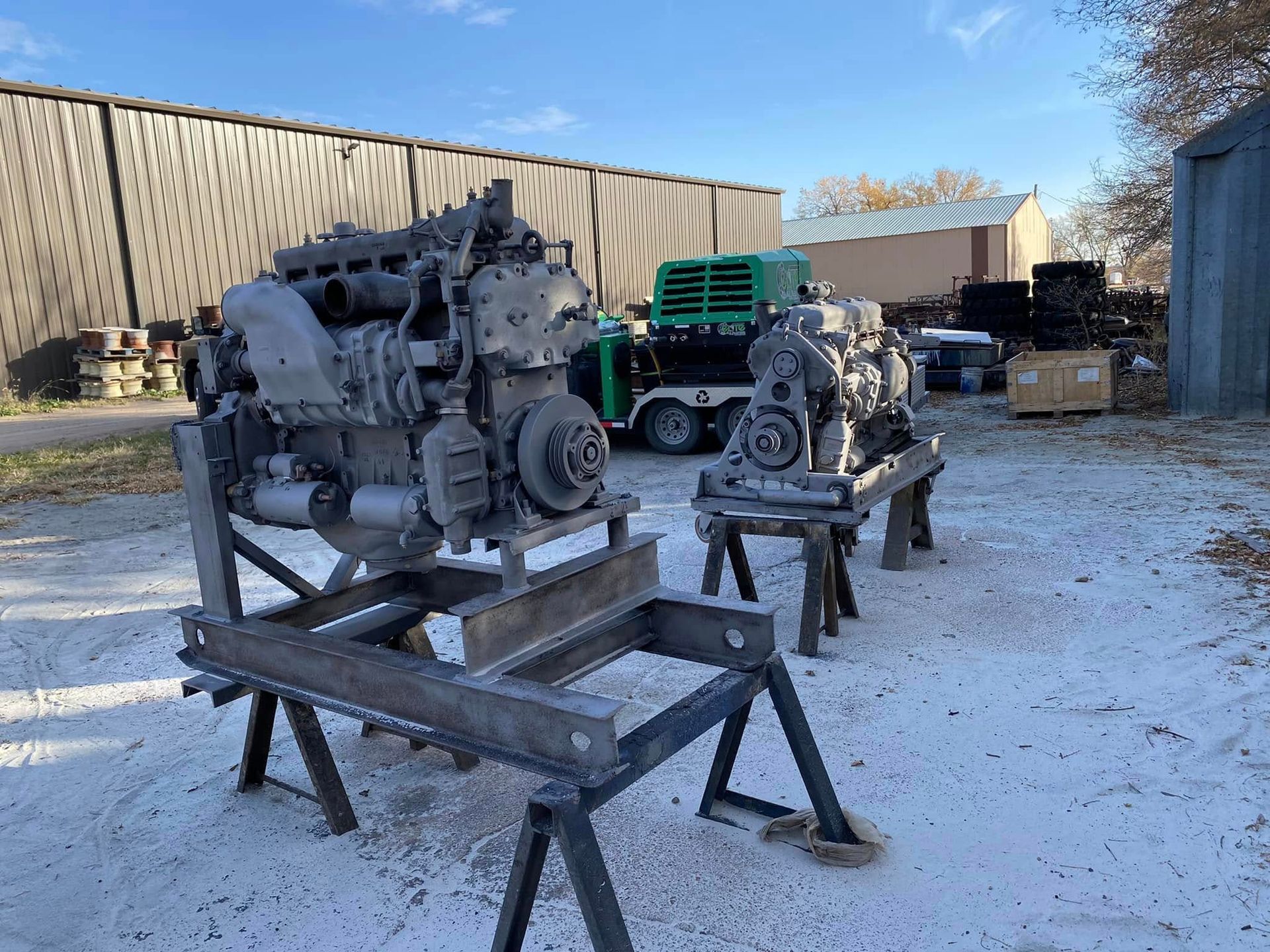 Two industrial engines on metal stands in a snowy outdoor yard with green truck in the background