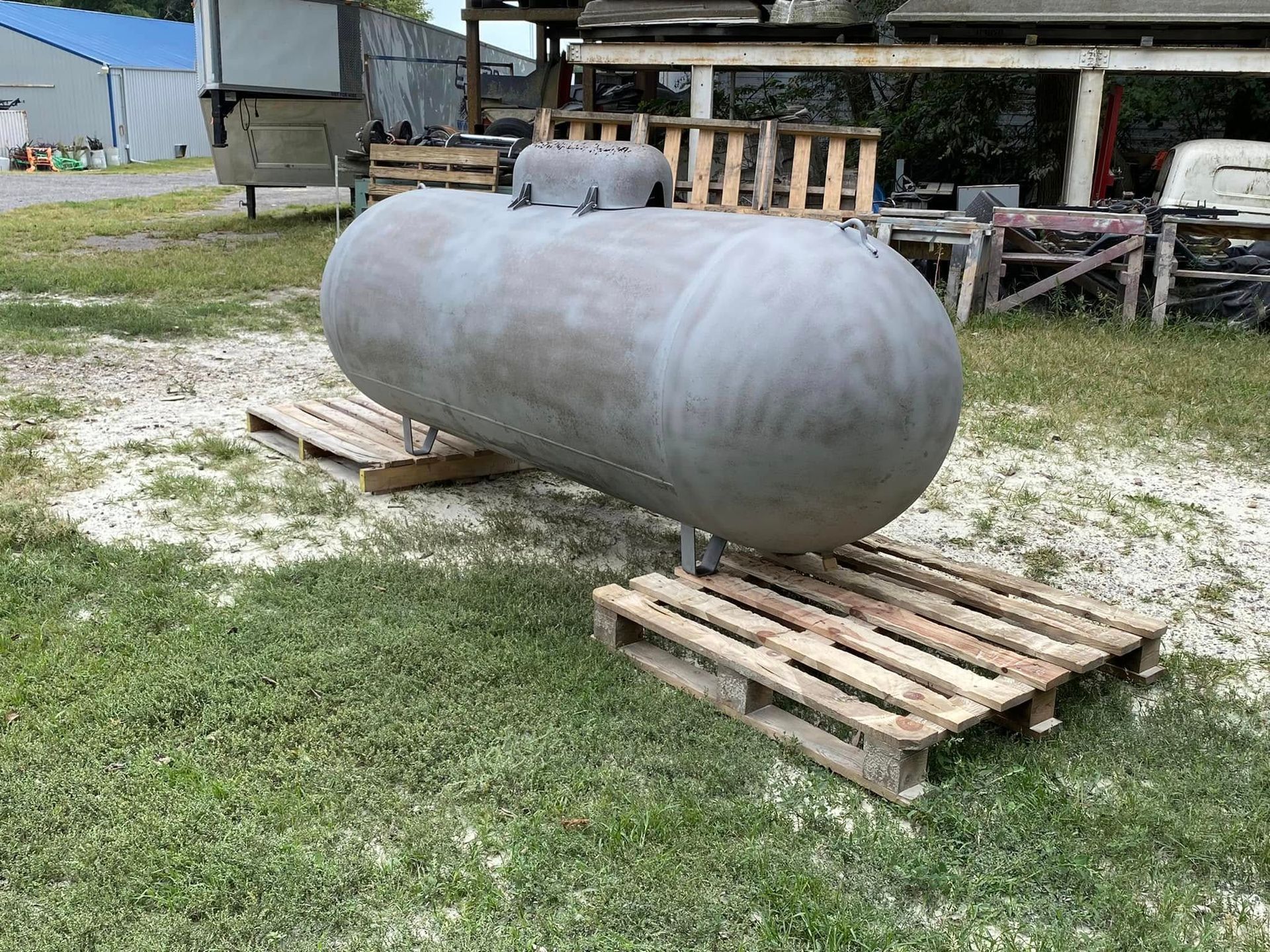Large gray cylindrical tank resting on wooden pallets outdoors in a grassy yard
