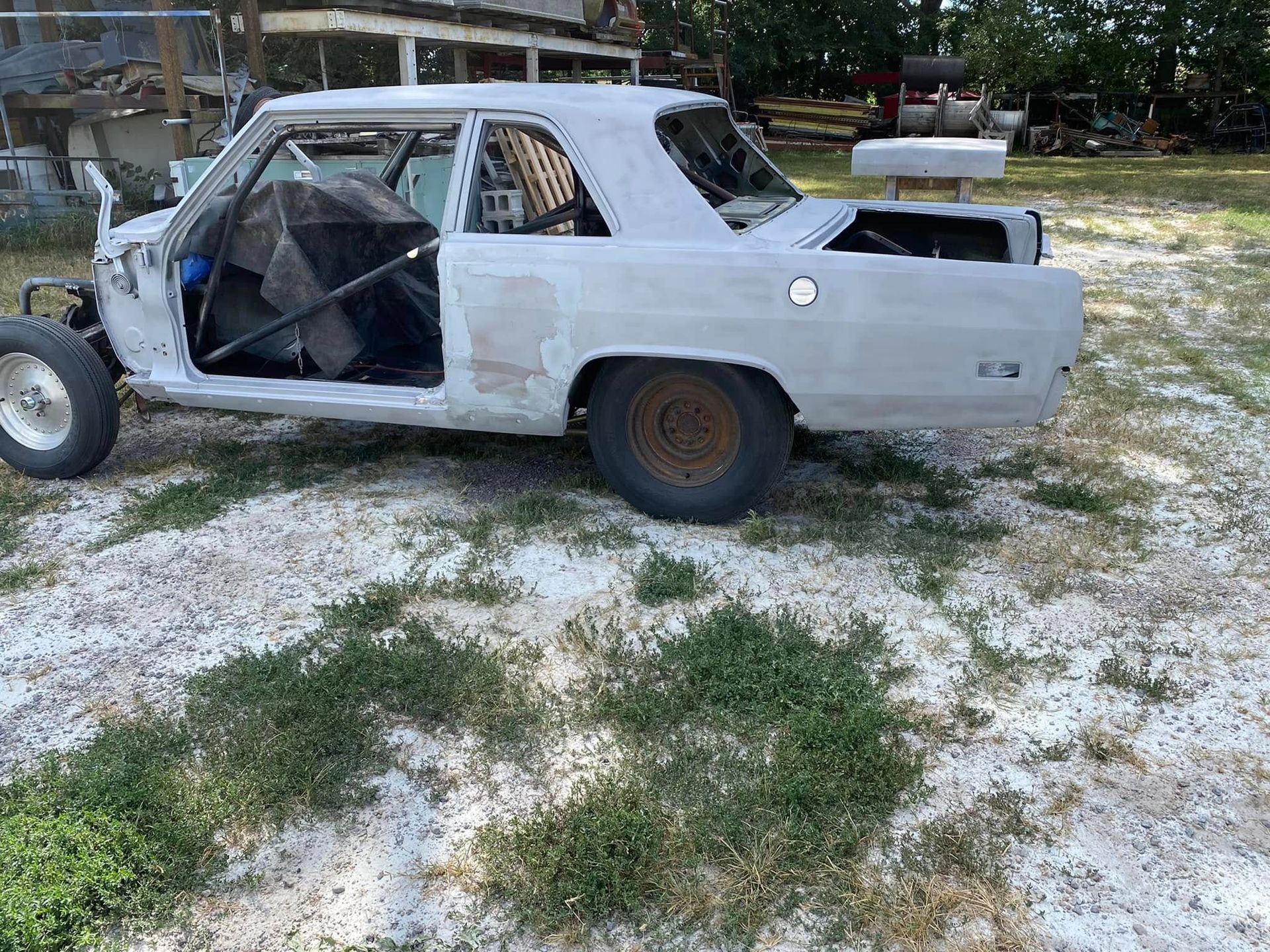 White race car shell with missing doors parked on grass, showing a stripped interior and roll cage.