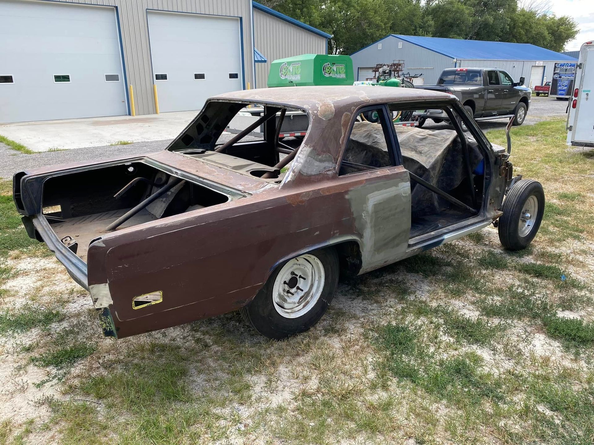 Partially stripped brown car body in a scrapyard, missing doors and windows