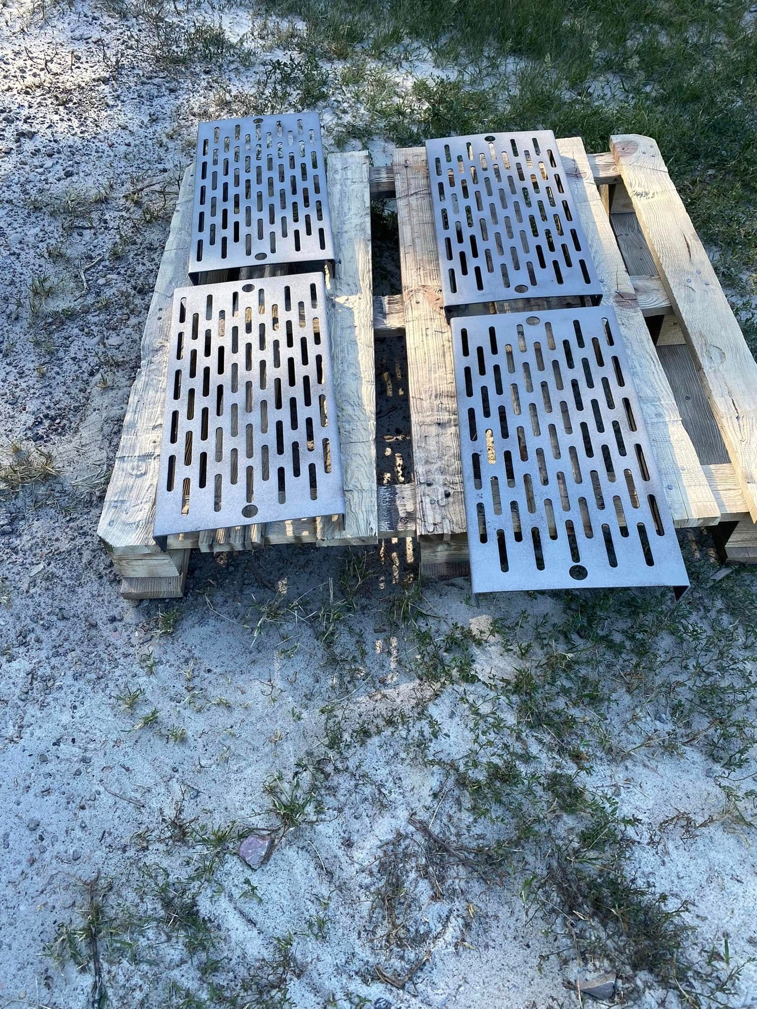 Two wooden pallets with metal grates on gravel, arranged side by side.