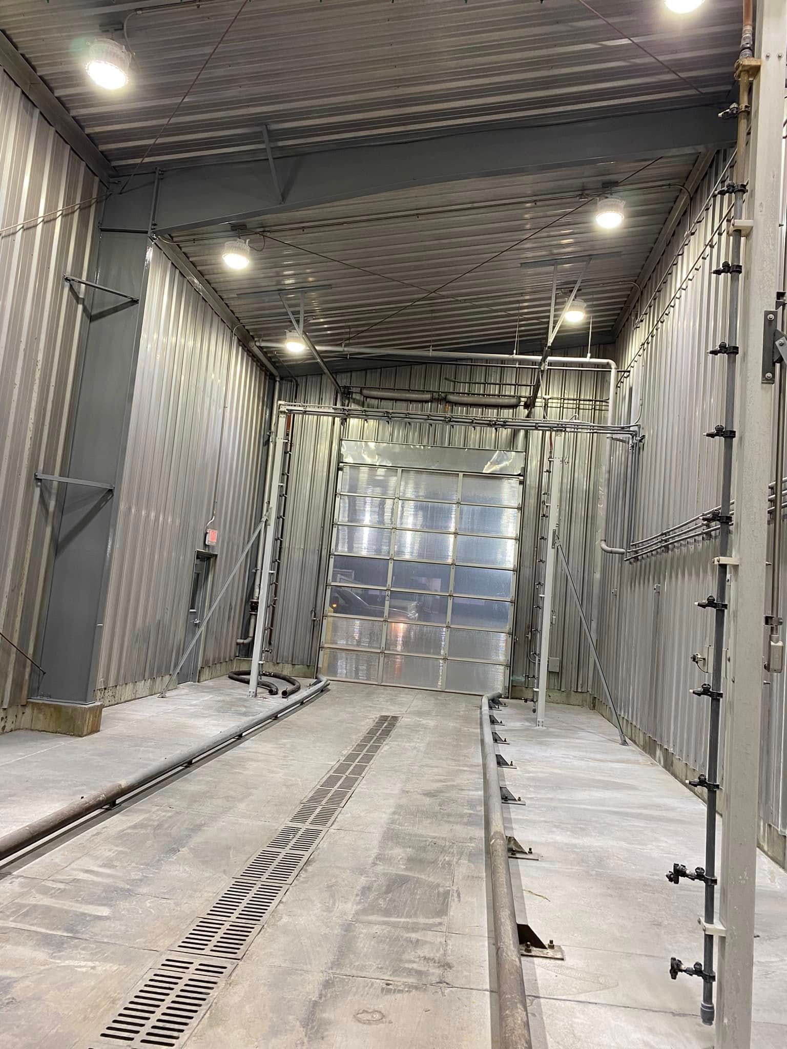Empty industrial truck wash bay with metal walls, floor tracks, and bright overhead lights