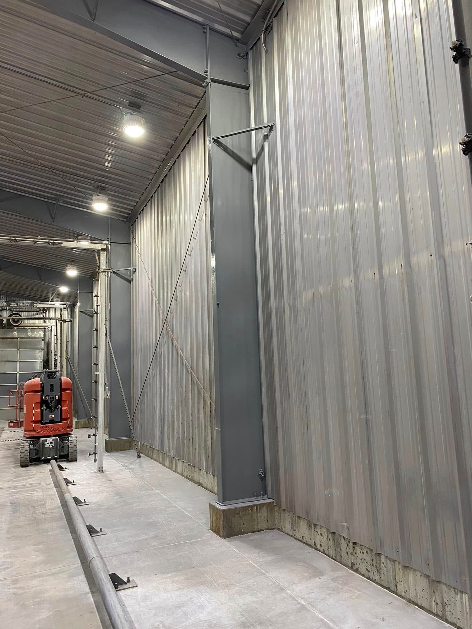 Industrial warehouse corridor with corrugated metal walls, overhead lights, and a red lift in the distance