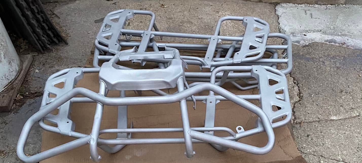 Stacked gray metal car frames on cardboard, with a rugged vehicle frame in the foreground.