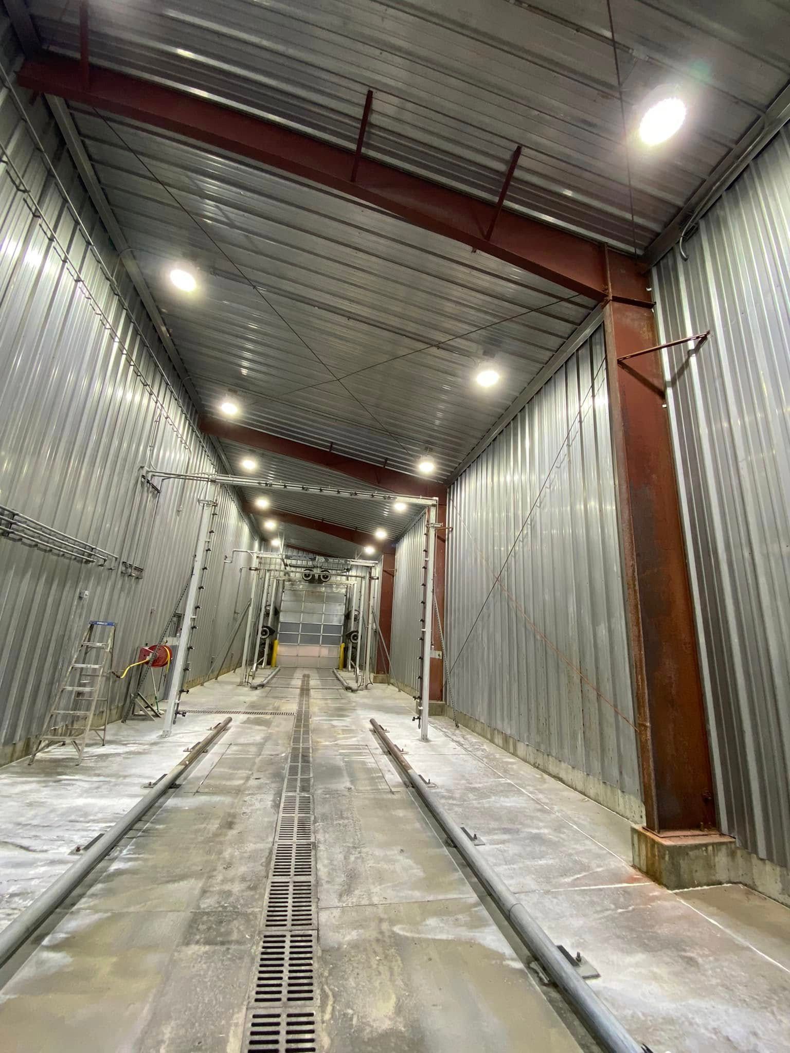Concrete tunnel-like corridor with metal walls, overhead lights, and a floor drainage channel