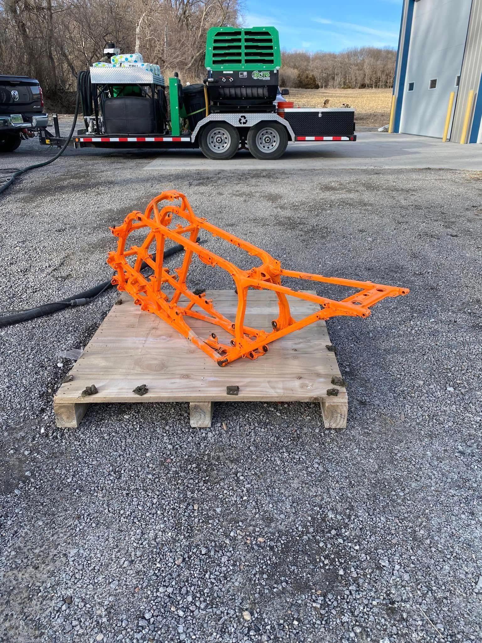 Orange metal cage on a wooden pallet in a gravel lot, with a truck in the background.