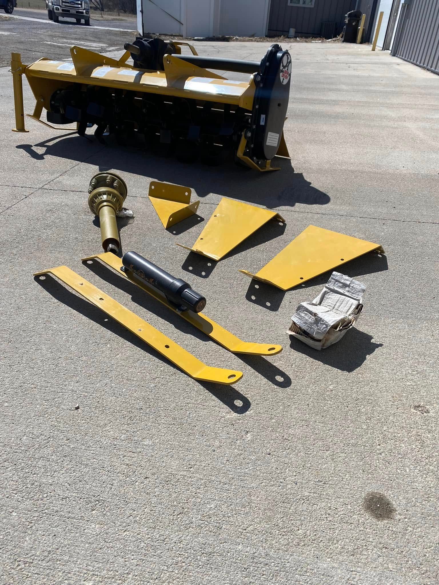 Yellow snow plow blades and parts laid out on pavement near a heavy-duty plow truck.