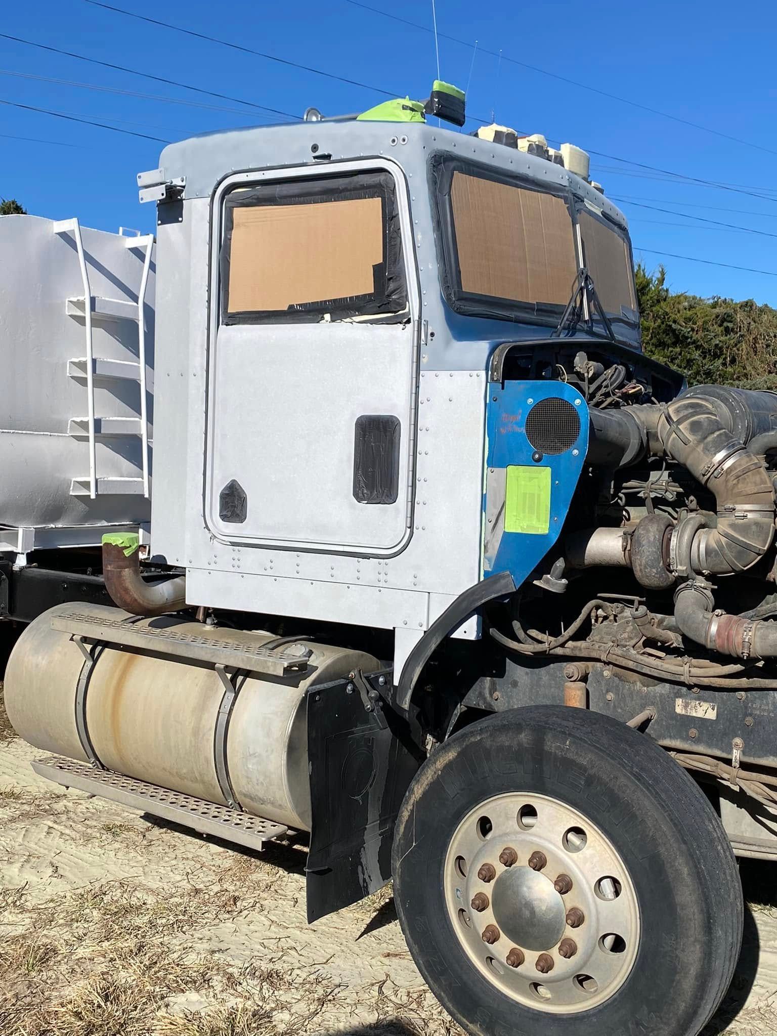 White semi-truck cab with blue engine parts parked outdoors under a clear sky.