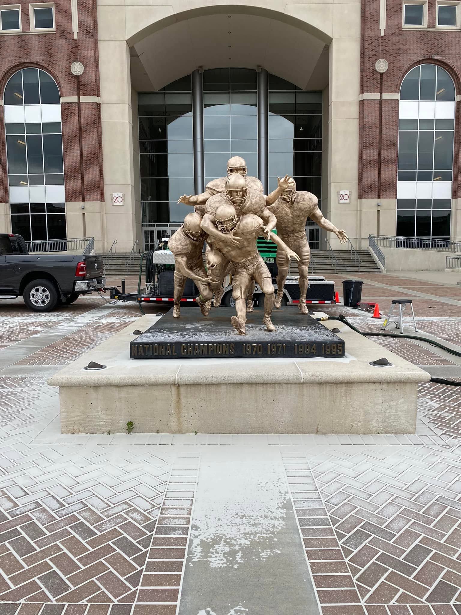 Bronze statue of three soldiers on a snowy plaza before a brick building entrance