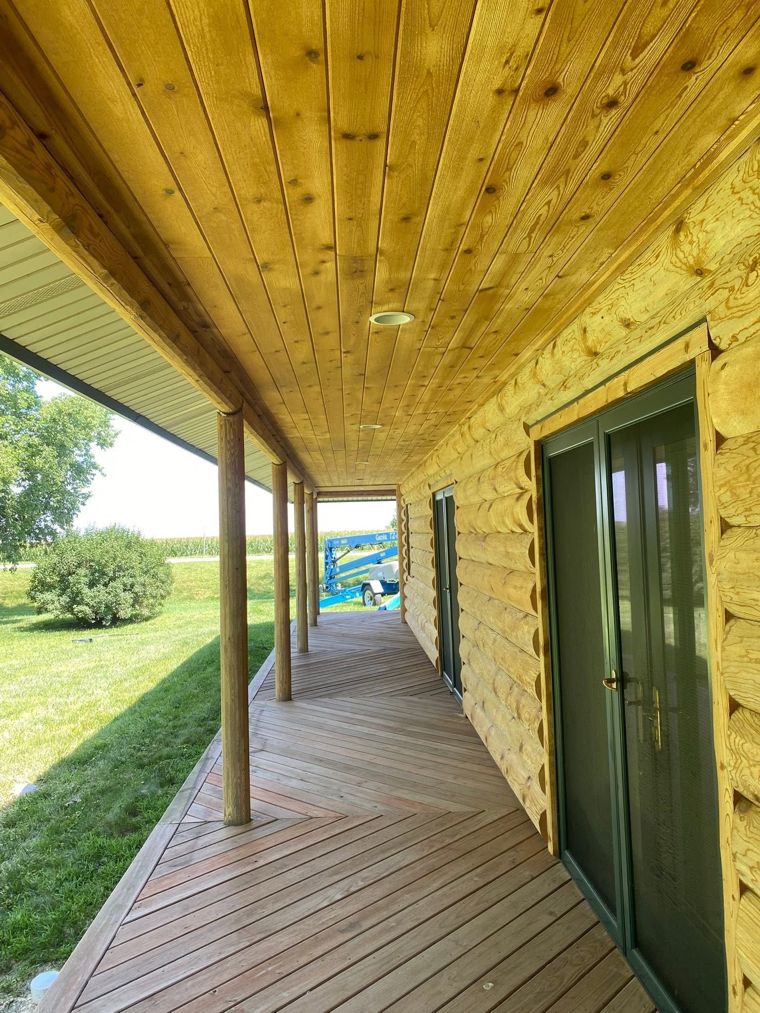 Covered wooden porch with slatted ceiling, green doors, and a view of the yard beyond.
