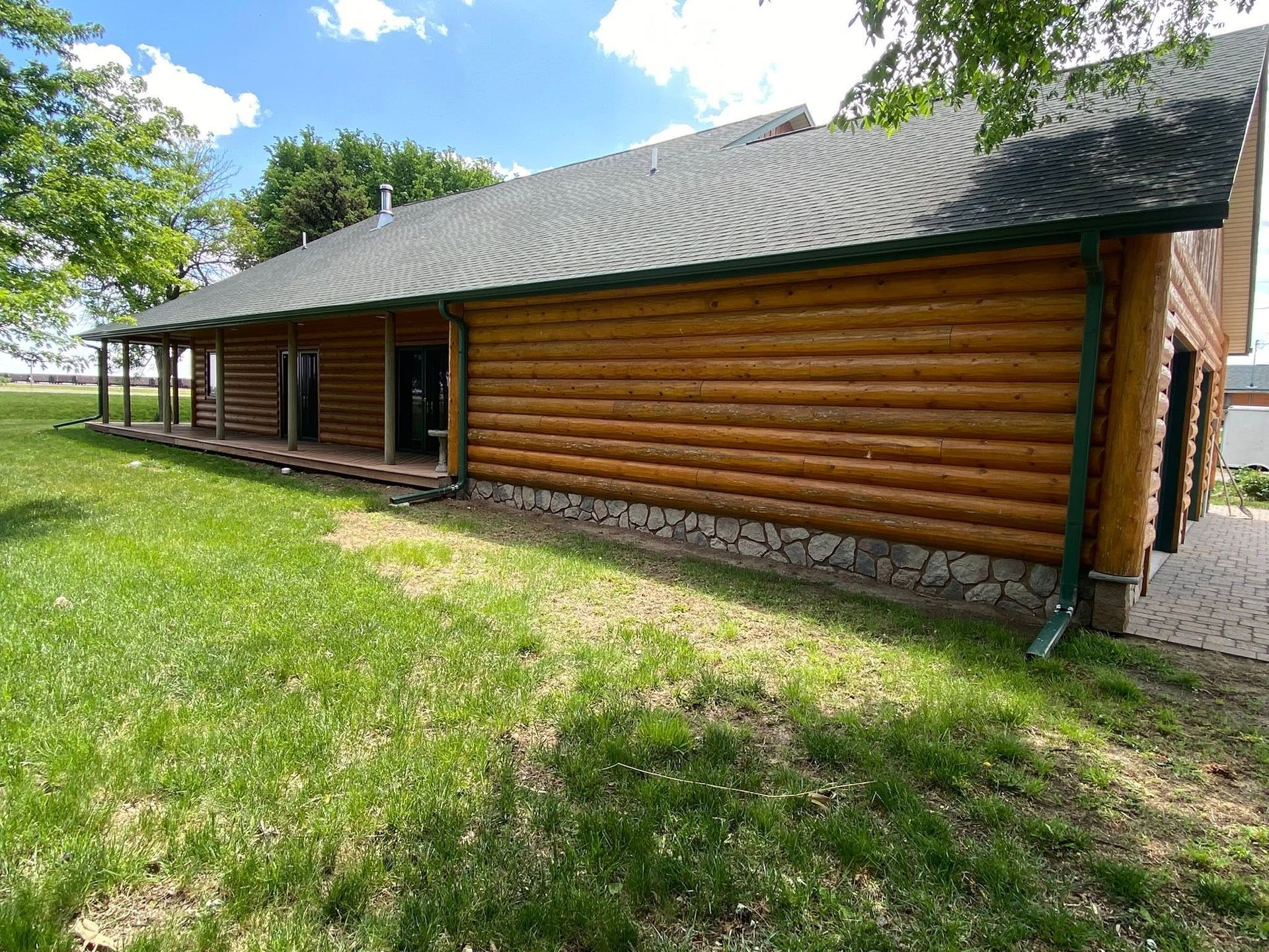 Log cabin with log walls and a dark roof beside a grassy lawn under a partly cloudy sky