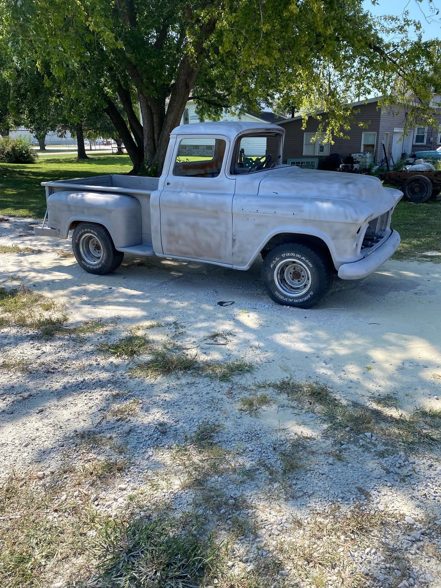 White vintage pickup truck parked on a gravel driveway under trees, with a house in the background