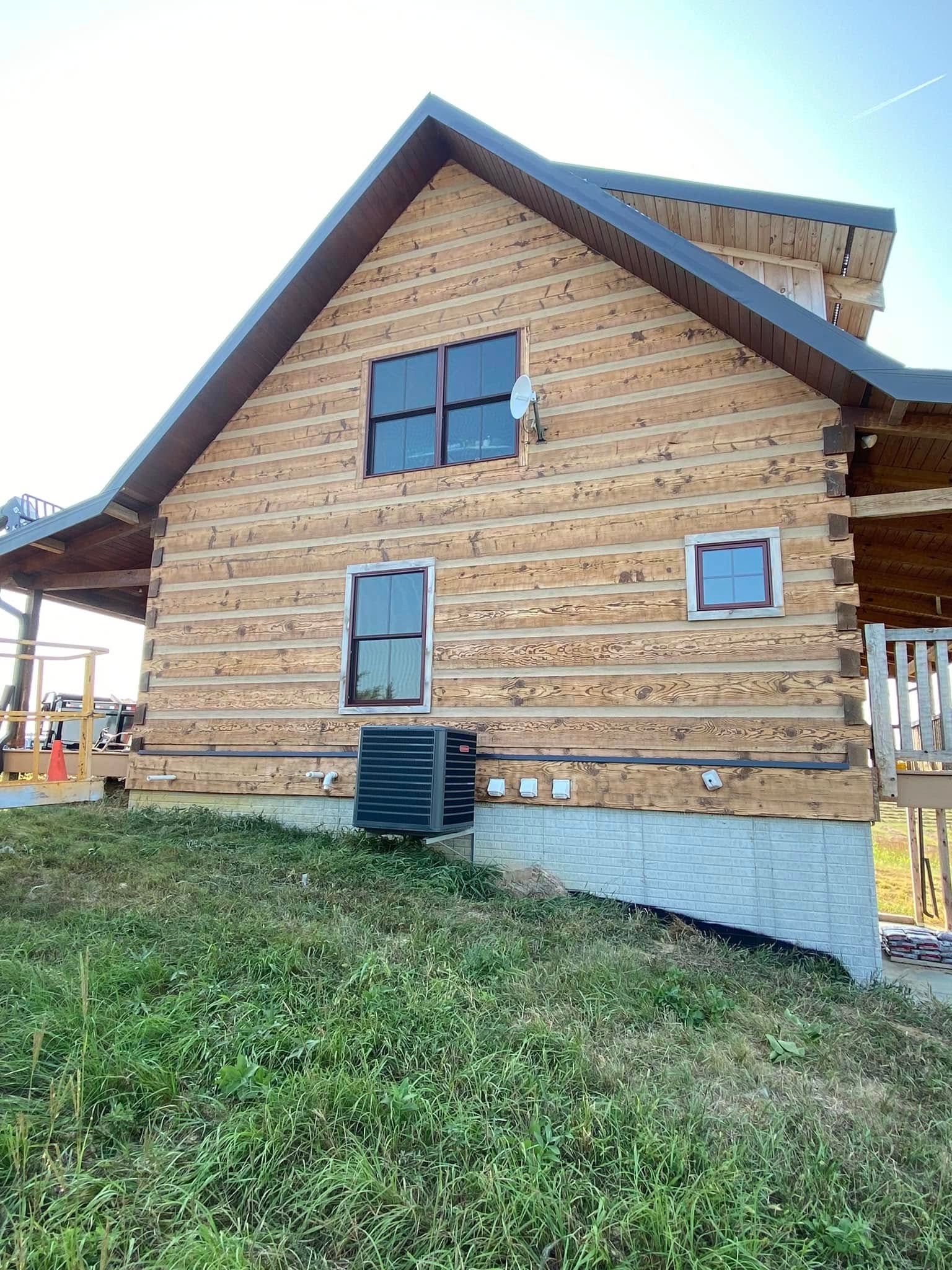 Wood-sided house with steep roof and large windows, viewed from the side in a grassy yard.