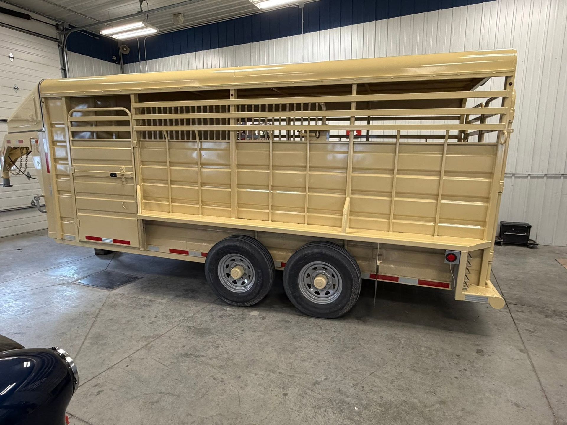 Tan enclosed tan livestock trailer with dual axles parked indoors in a warehouse