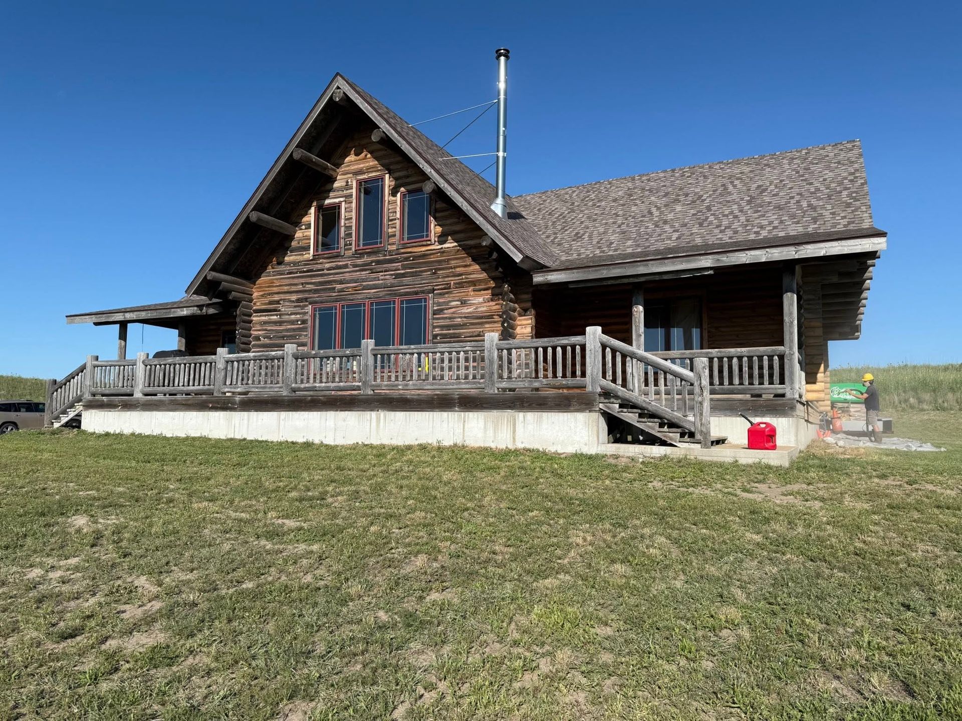 Rustic wooden cabin with a porch and ramp in a grassy field under a clear blue sky