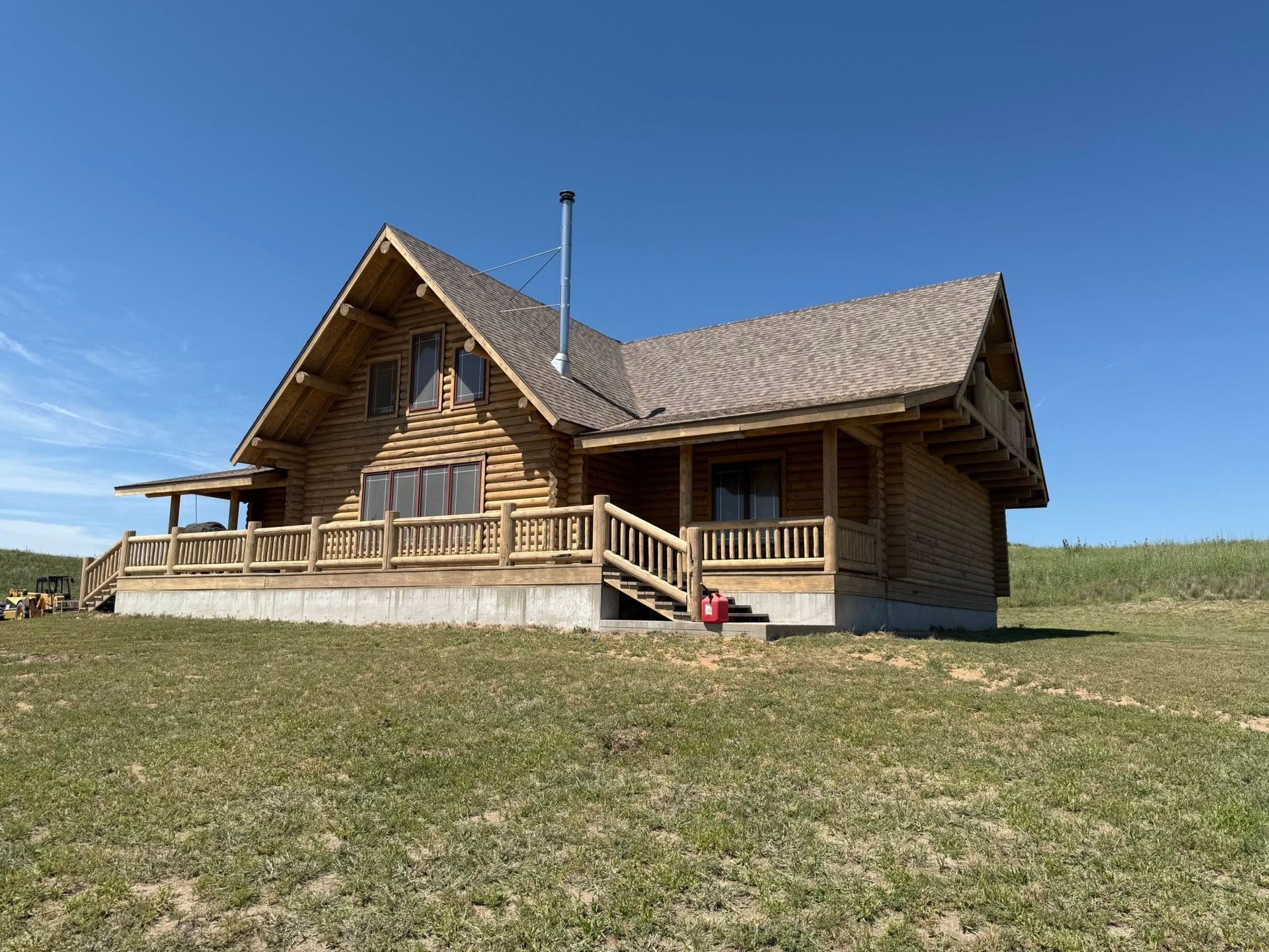 Rustic wooden cabin with a porch on a grassy hill under a clear blue sky