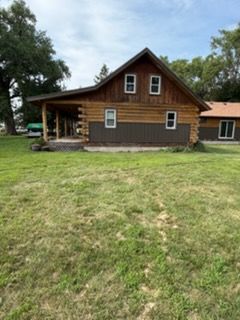 Wooden house with brown siding and a large grassy yard, viewed from the front.