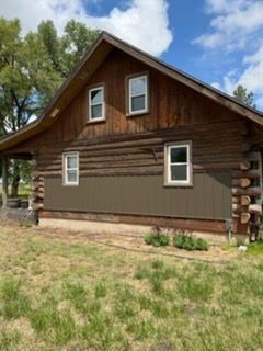 Rustic brown wooden house with green siding, white-trimmed windows, and a grassy yard under a blue sky.