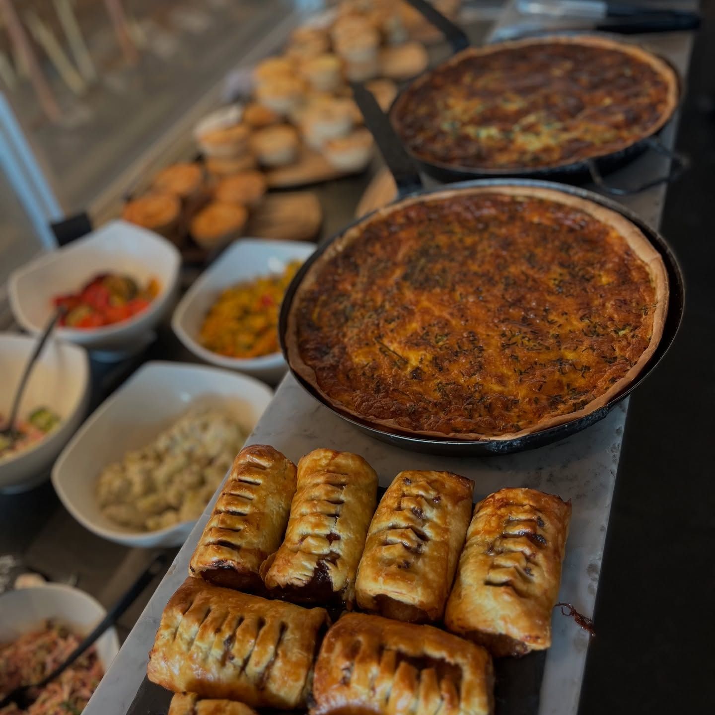 Buffet of baked dishes and pastries on a countertop, with bowls of side dishes in the background