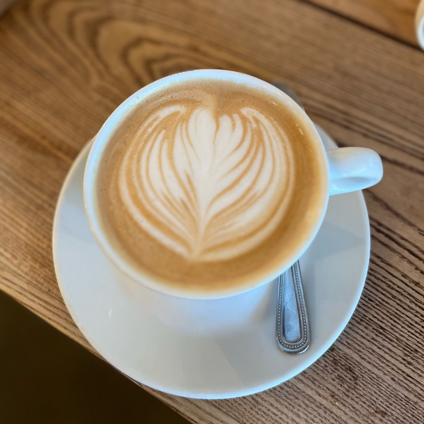 Latte with leaf latte art on a white saucer on a wooden table
