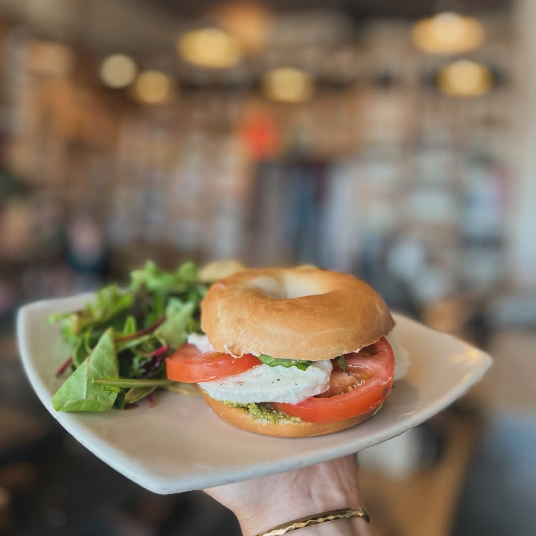 Hand holding a sandwich on a plate with greens in a softly blurred café setting