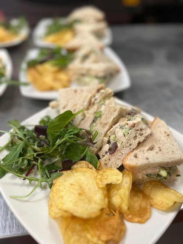 Sandwich triangles with salad greens and potato chips on a white platter, with more plates blurred behind