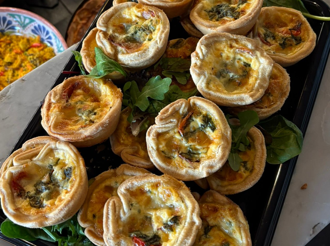 Tray of golden baked mini quiches with herbs, arranged on lettuce leaves.