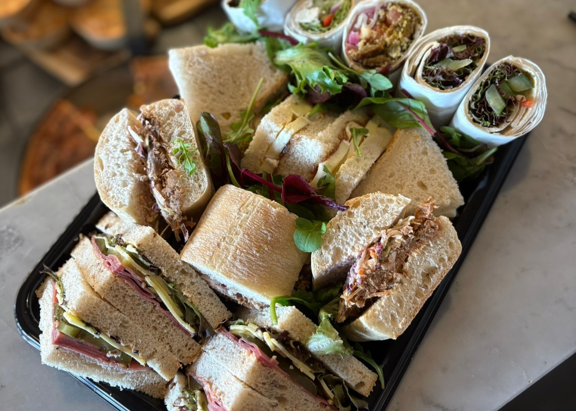 Assorted finger sandwiches and sushi rolls on a black tray, garnished with greens