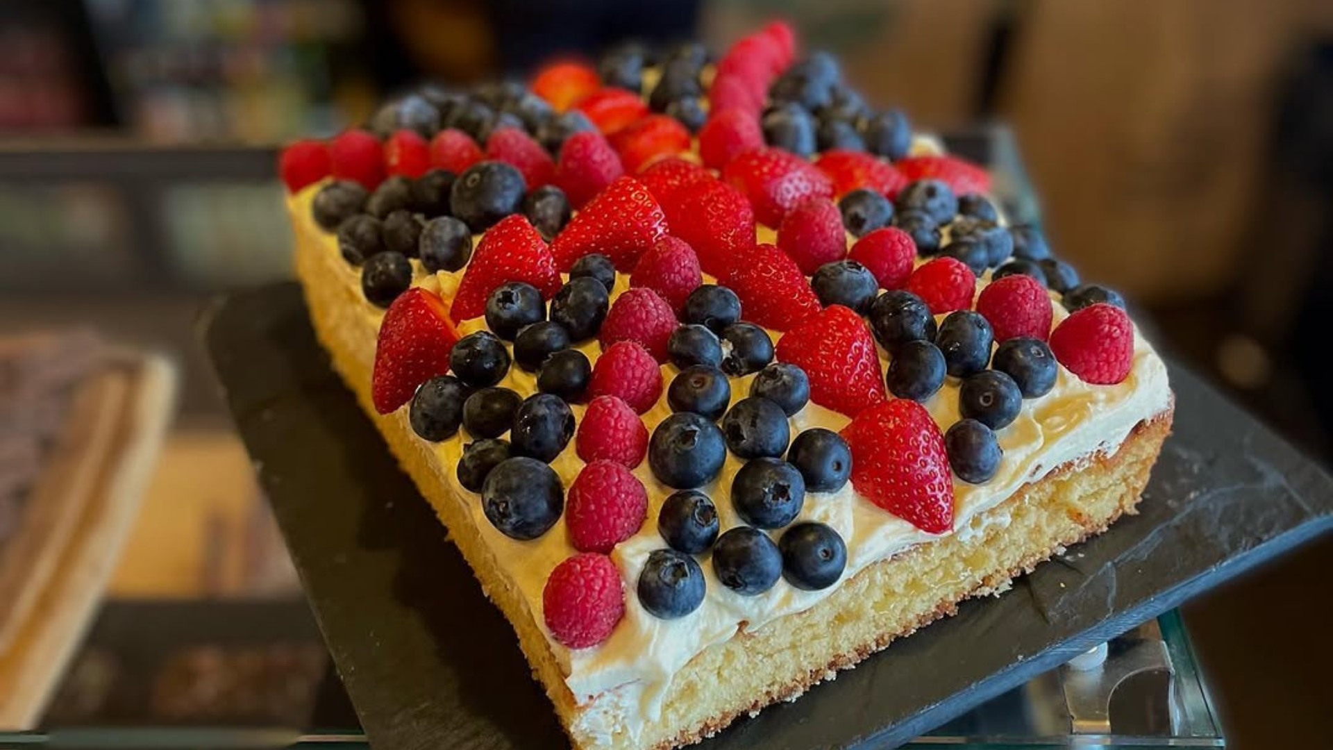 Square berry-topped cake with raspberries, blueberries, and blackberries on a dark serving tray