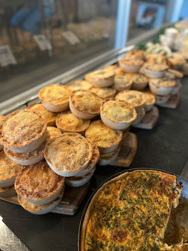 Rows of small savory pies in clear cups beside a large quiche on a bakery display counter